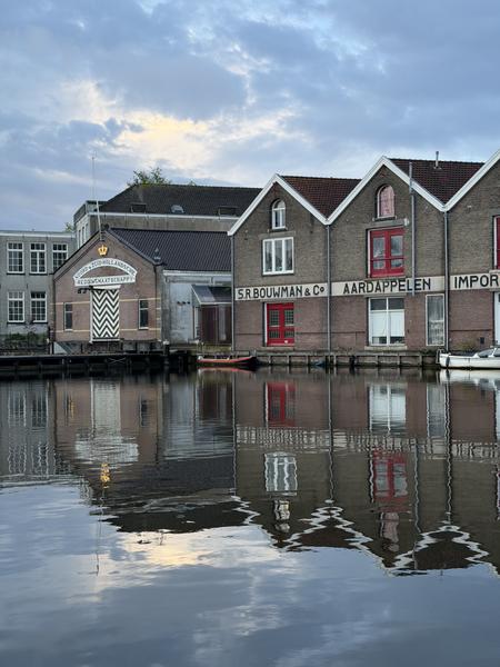 This tranquil photo captures the historic canal houses of Marinierskade, Kattenburg, Amsterdam, with their detailed facades and vibrant red accents reflected perfectly in the calm water below